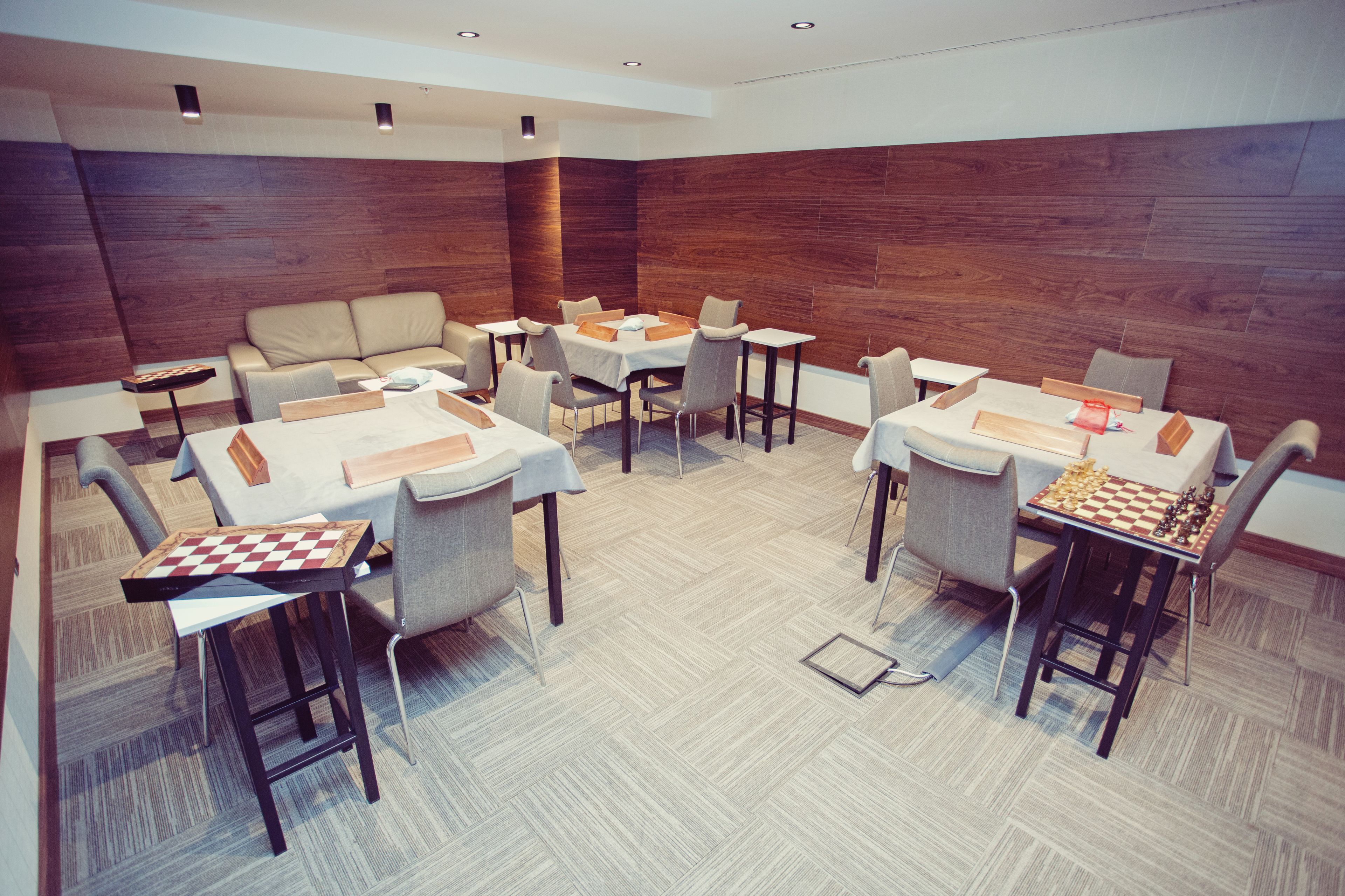 Un comedor moderno con varias mesas y sillas, paneles de madera en las paredes y un patrón de suelo en espiga.