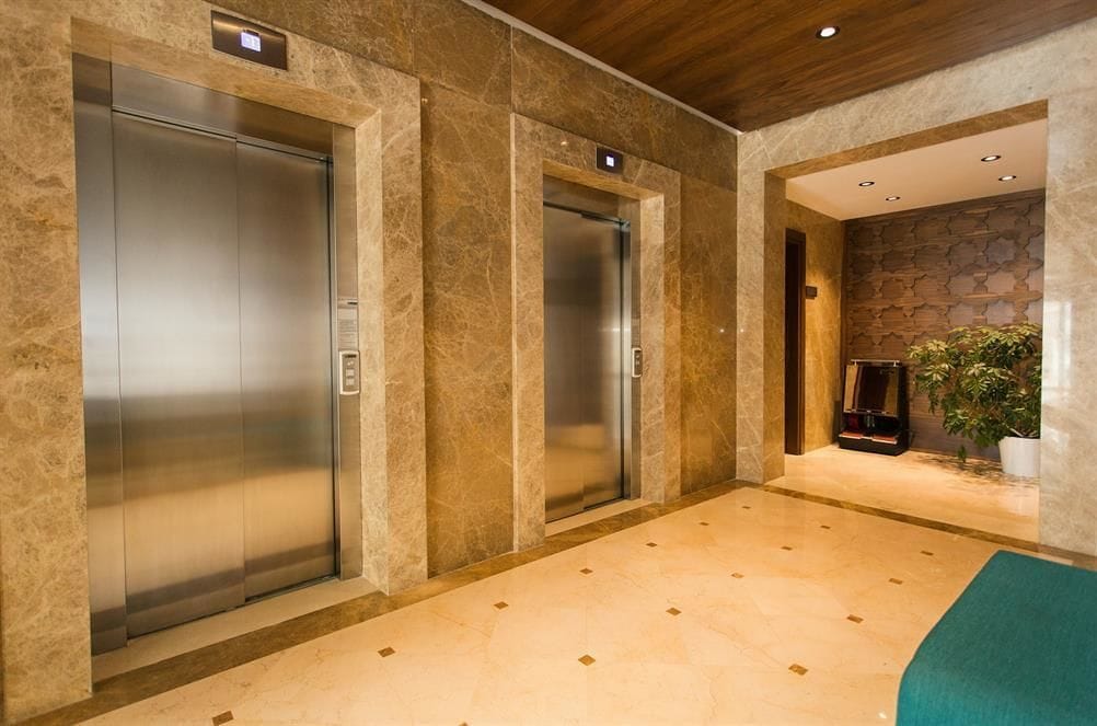 A modern elevator area with two elevators, marble walls, and a stone wall with a plant.