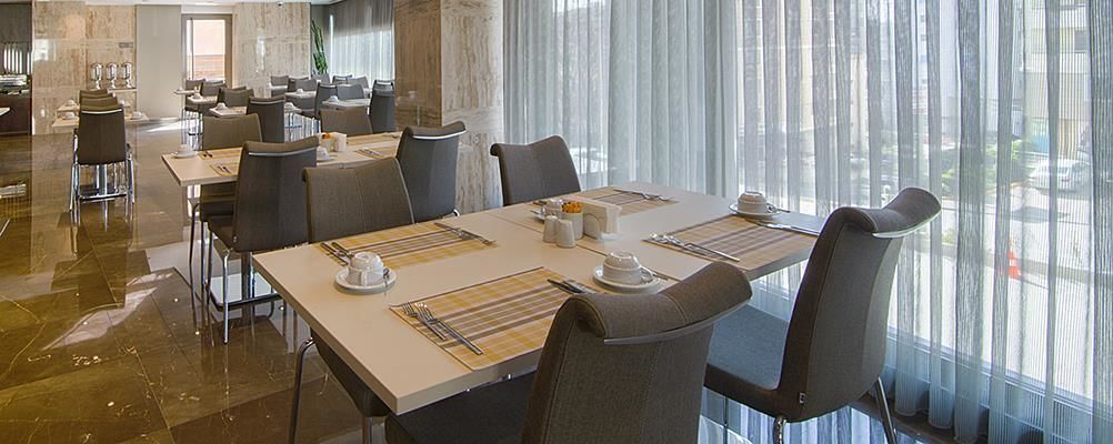 Comedor con mesas dispuestas para cuatro, sillas y un amplio ventanal con cortinas.