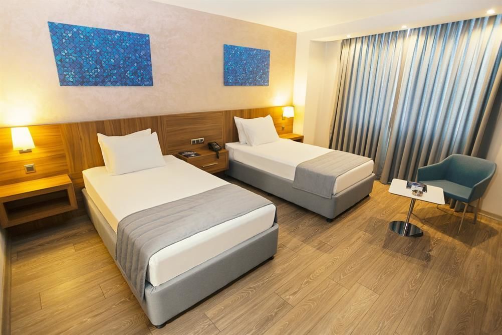 Una habitación de hotel con dos camas, una mesita pequeña, una silla y obras de arte en las paredes.