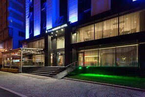 Un hotel para negocios con fachada de vidrio, entrada cubierta e iluminación exterior.