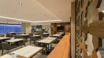 A modern restaurant with a long counter and multiple tables, a wooden accent wall, and a view of the city.