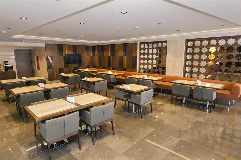 A modern hotel lobby with multiple seating areas, including tables and sofas, and a decorative wall with patterned panels.