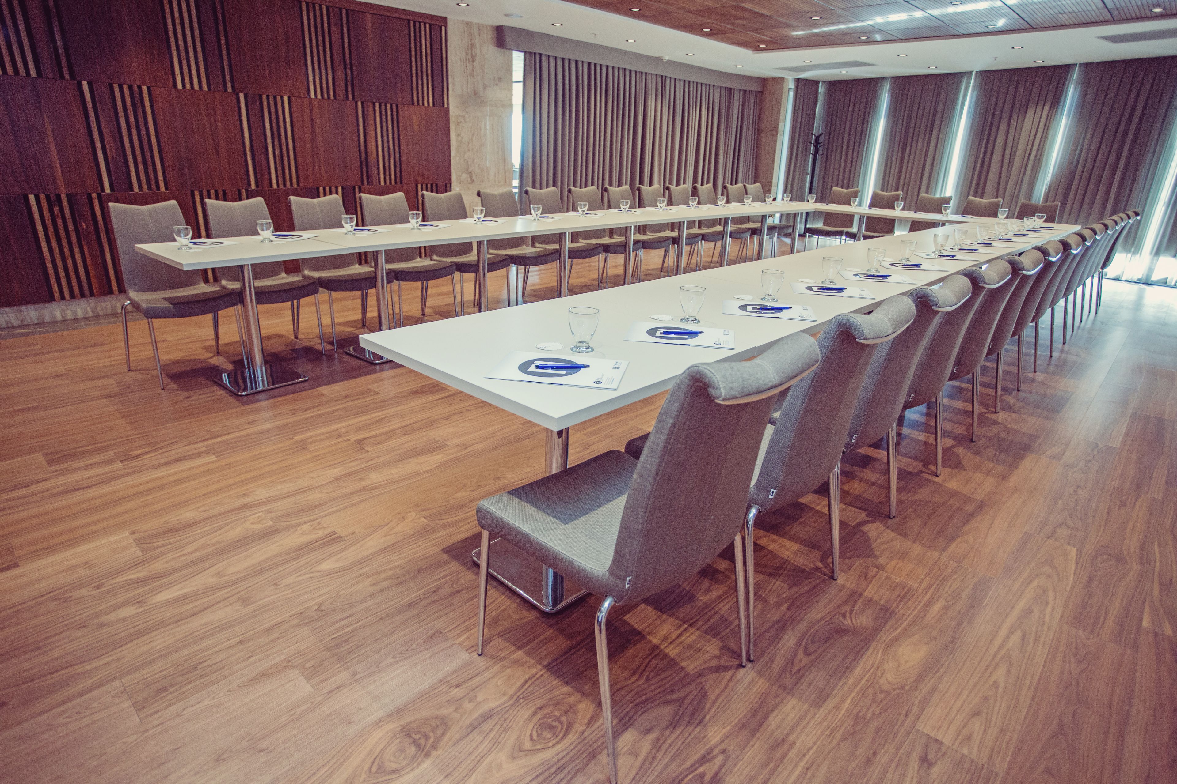 A conference room with long tables and chairs, wooden floors, and a modern design.
