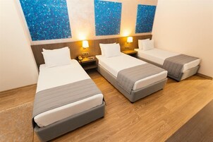 A hotel room with three single beds, wooden flooring, and blue decorative wall art.