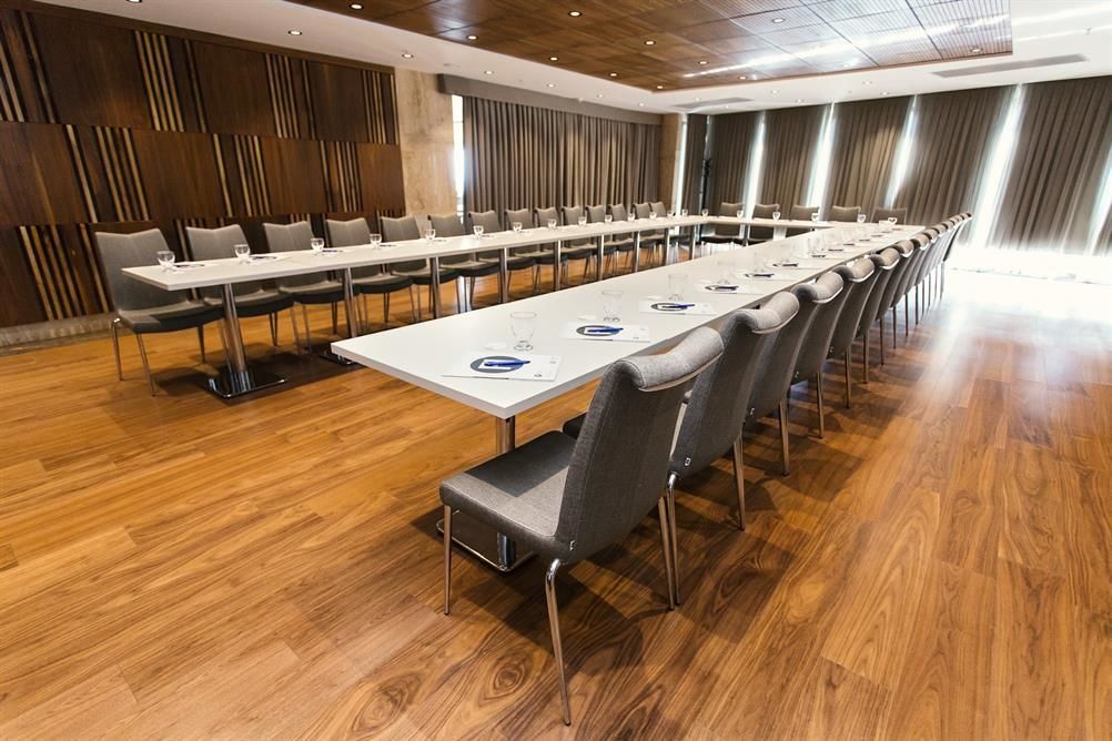 Een vergaderruimte met een lange tafel, stoelen en een houten vloer.