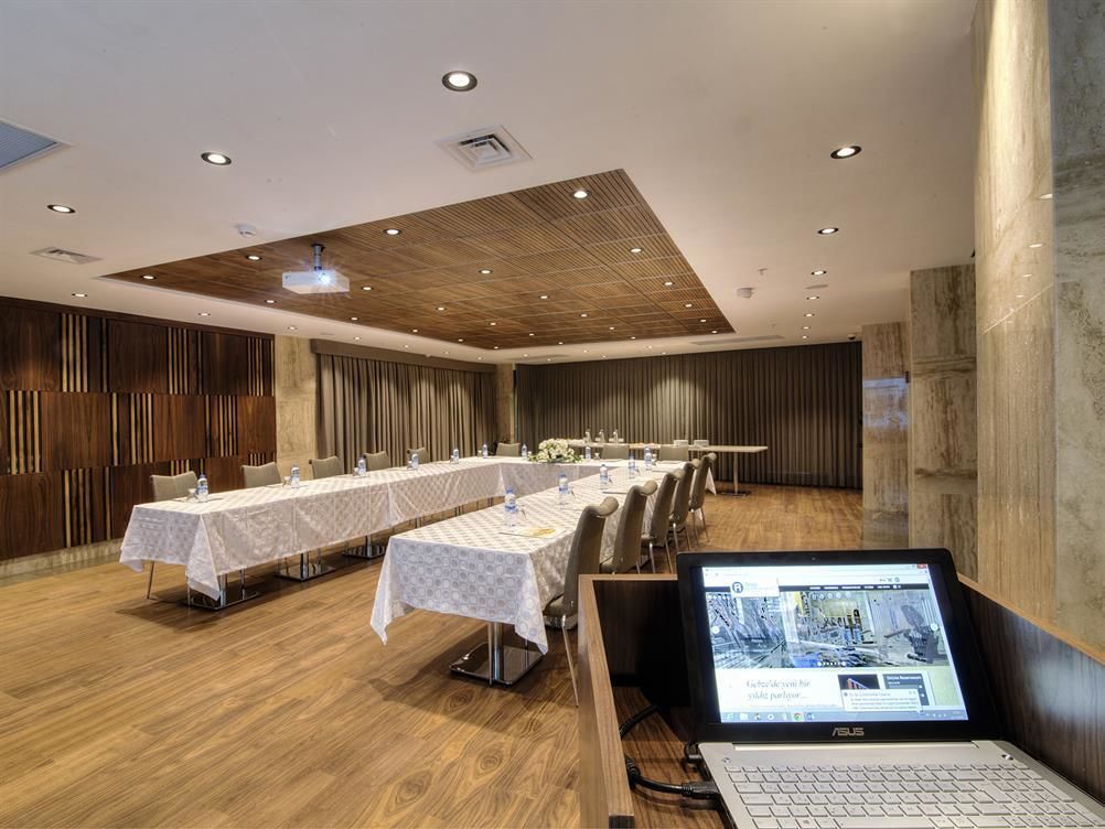 A conference room with long tables, a laptop on a stand, and wooden paneling on the walls.