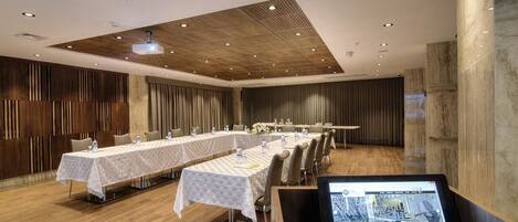 A conference room with long tables, a laptop on a stand, and wooden paneling on the walls.