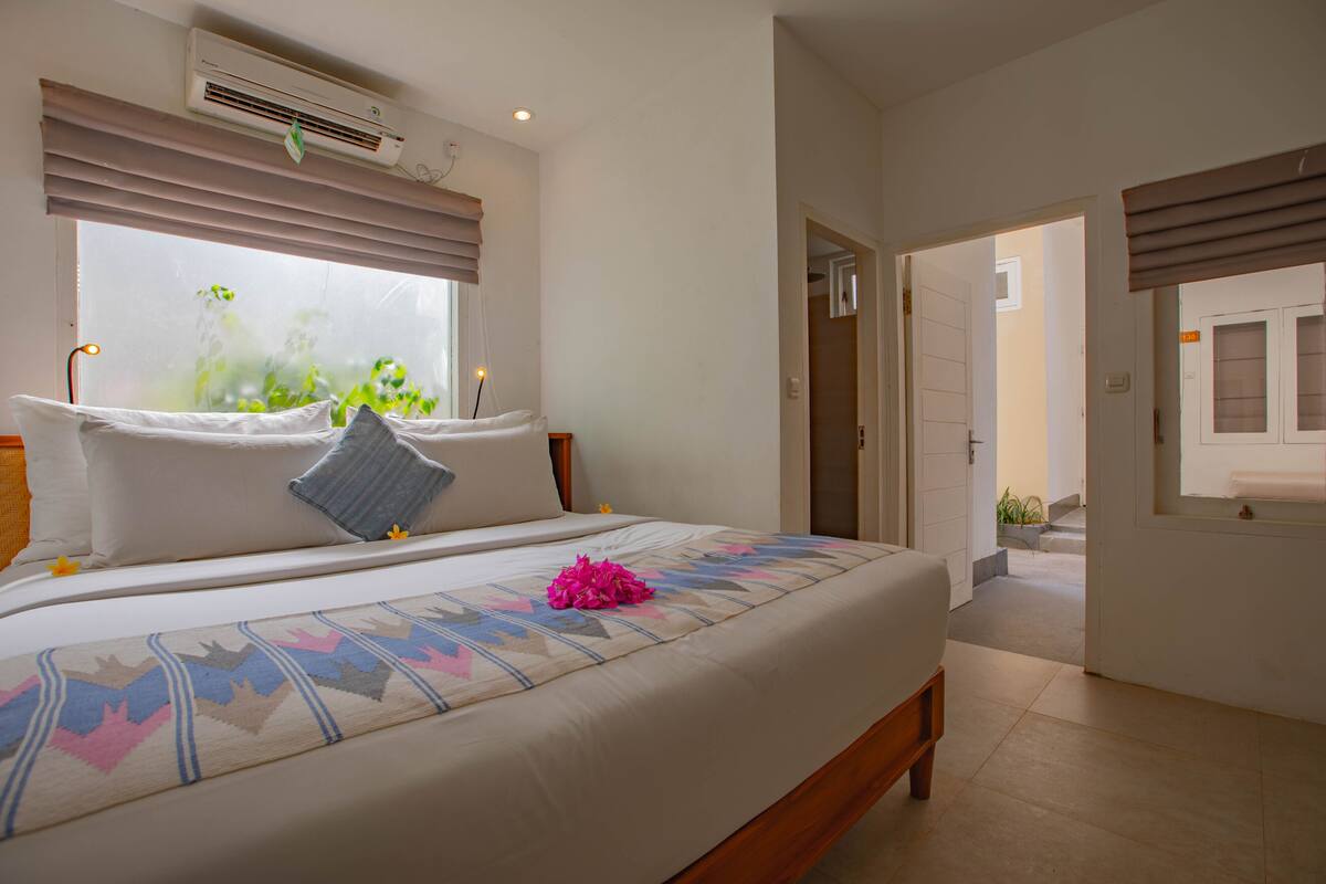 A bedroom with a large bed, an air conditioning unit, and a window with blinds.