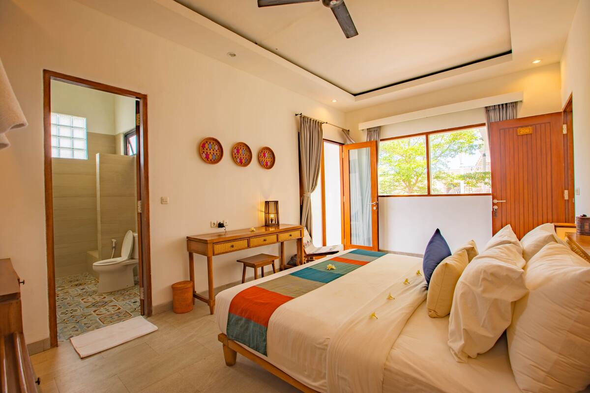 A bedroom with a bed, a desk, a chair, a mirror, and a window.