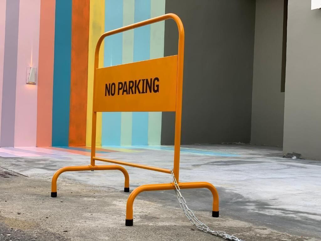 A "NO PARKING" sign in an indoor setting with colorful vertical stripes in the background.