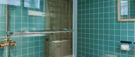 Ein Badezimmer mit türkisblauen Fliesen, einer Duschkabine aus Glas, einem Handtuchhalter und einem Spiegel.