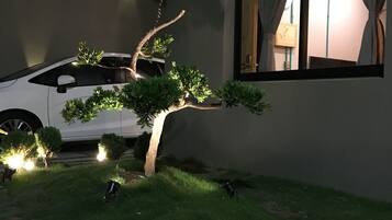 A white car parked in front of a building with a large rock in the foreground and a small tree with lights.