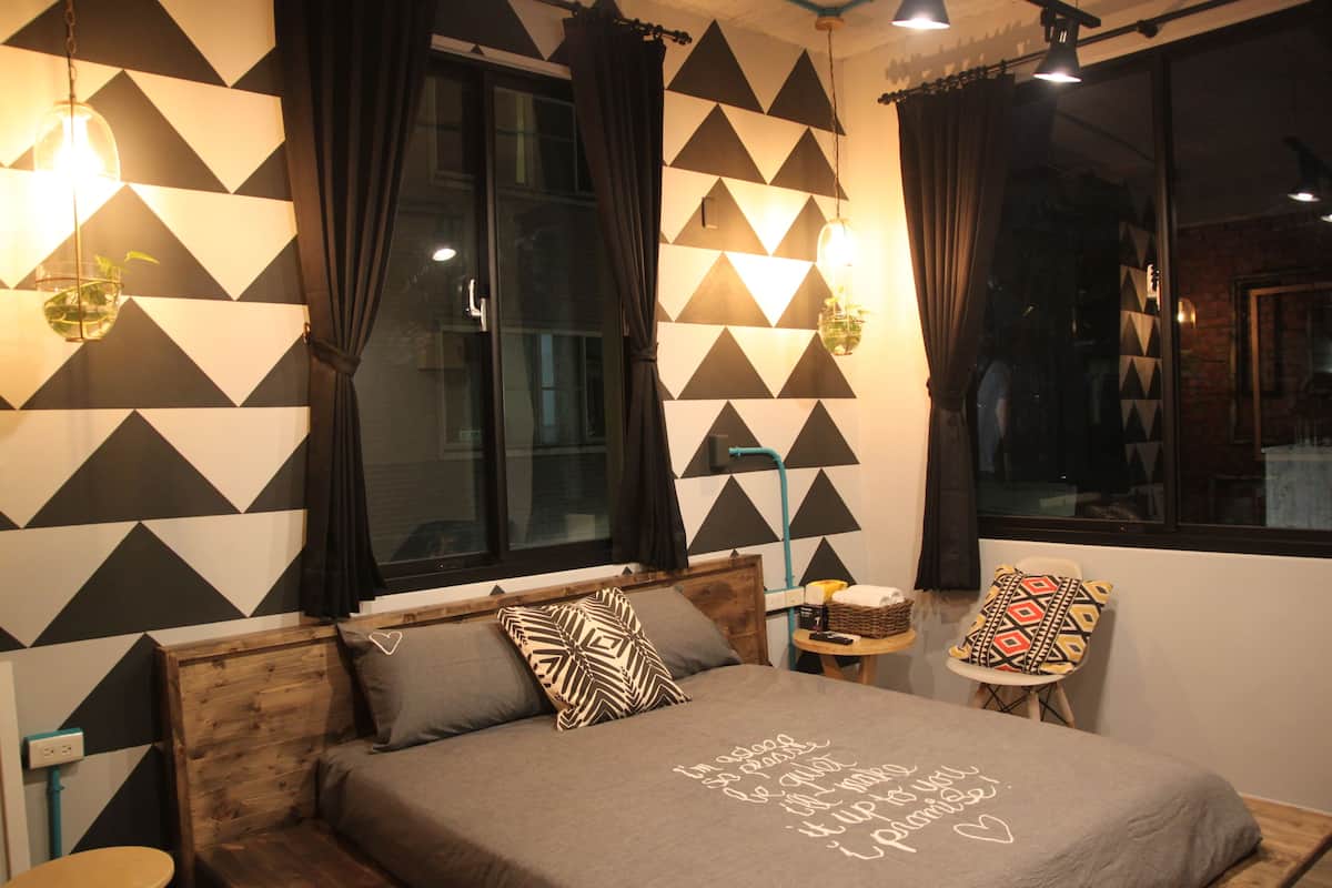 A bedroom with a bed, a wooden headboard, a nightstand, a chair, and a wall with geometric patterns.