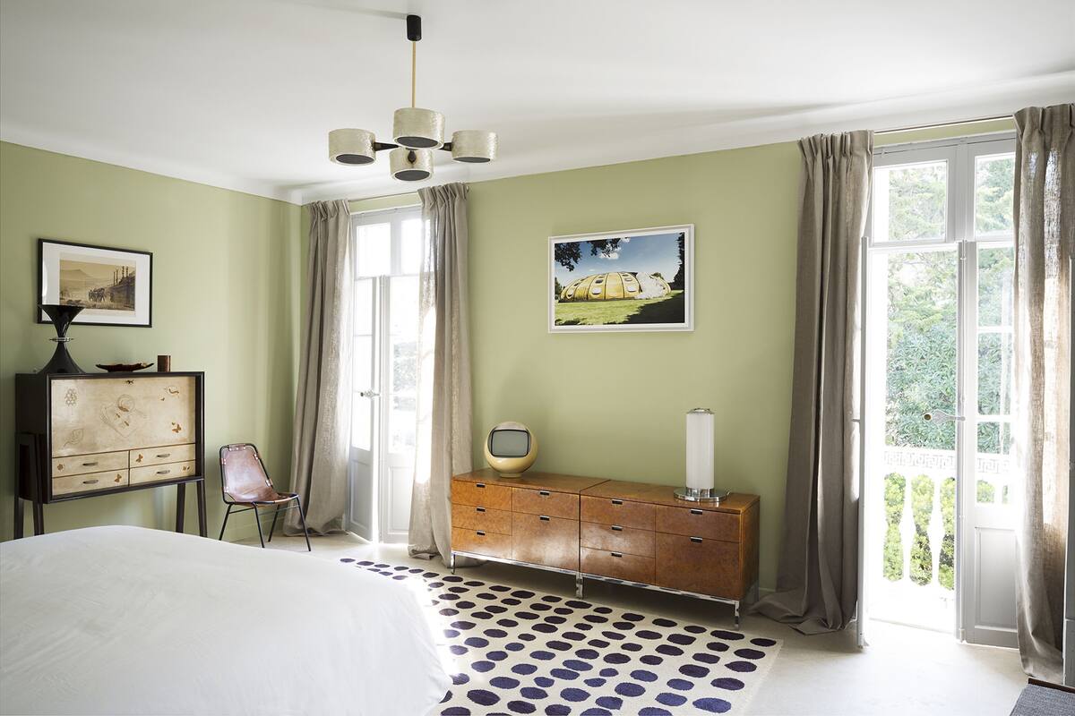 A bedroom with a bed, a dresser, a chair, a picture on the wall, and a window with curtains.