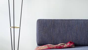 A sofa with a patterned throw, a floor lamp with three white shades, and a wooden floor.
