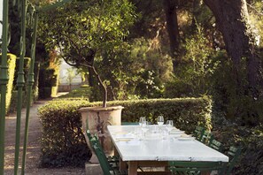 Une table installée à l’extérieur, avec des chaises, entourée de verdure et d’arbres.
