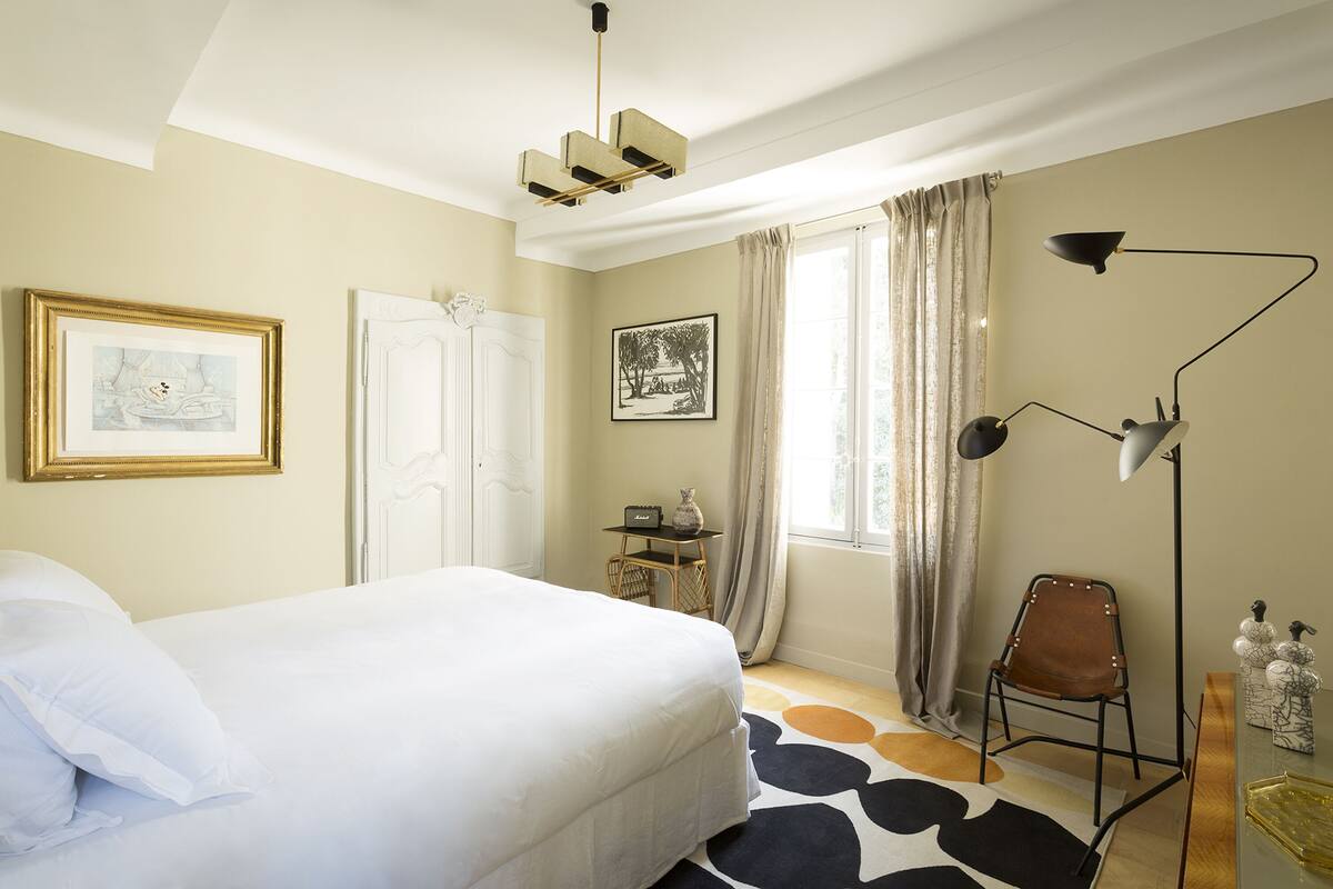 A bedroom with a bed, a desk, a chair, a floor lamp, and two framed pictures on the wall.