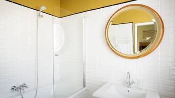 Une salle de bain moderne avec une douche à parois de verre, un miroir rond doté d’un cadre en bois et un lavabo blanc.