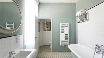 A bathroom with a white bathtub, a large mirror, and a tiled floor.