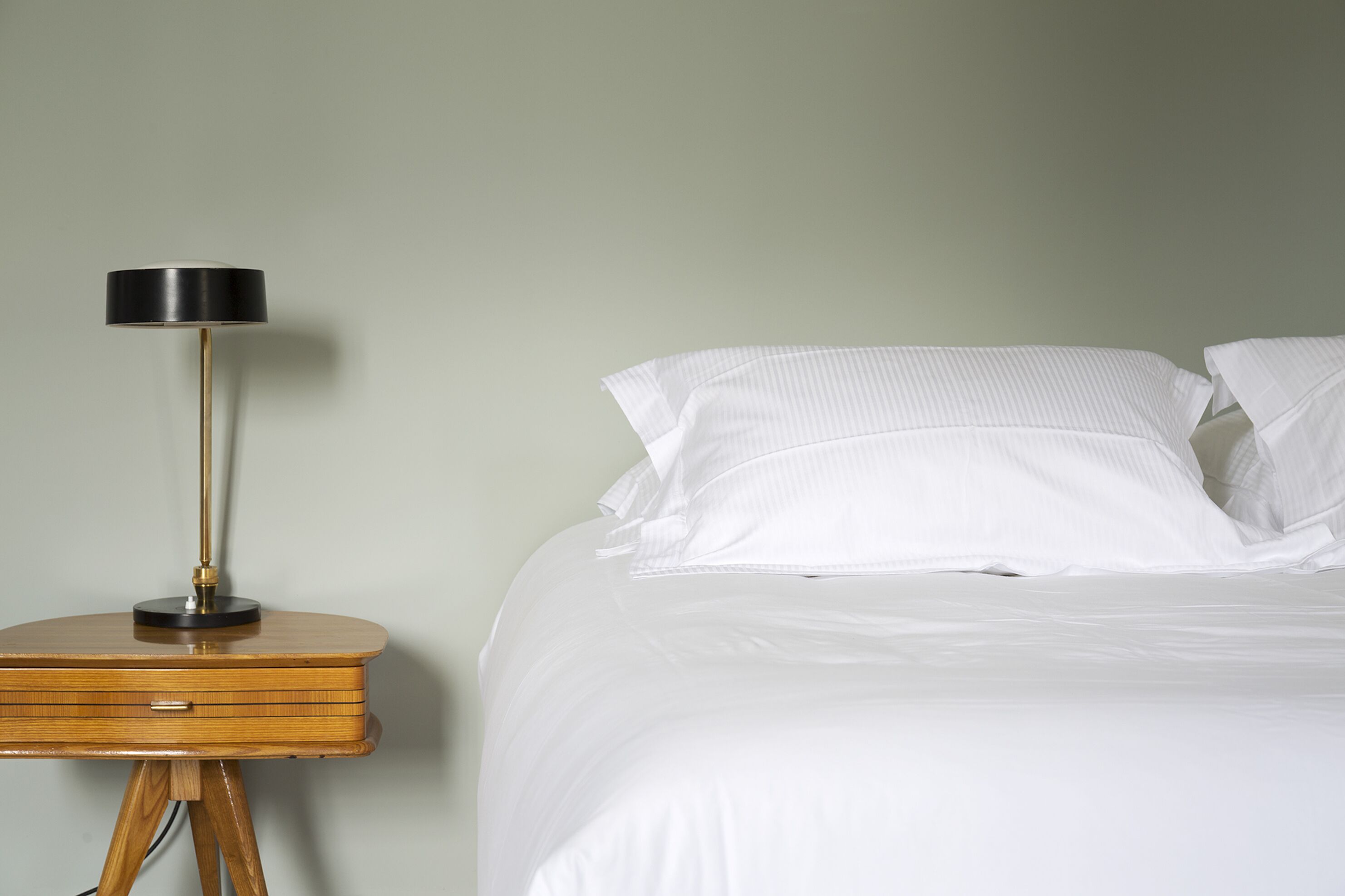 A bed with white bedding and pillows, a bedside table with a lamp, and a wooden nightstand.