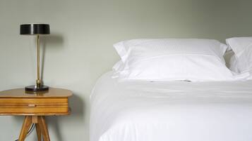 A bed with white bedding and pillows, a bedside table with a lamp, and a wooden nightstand.
