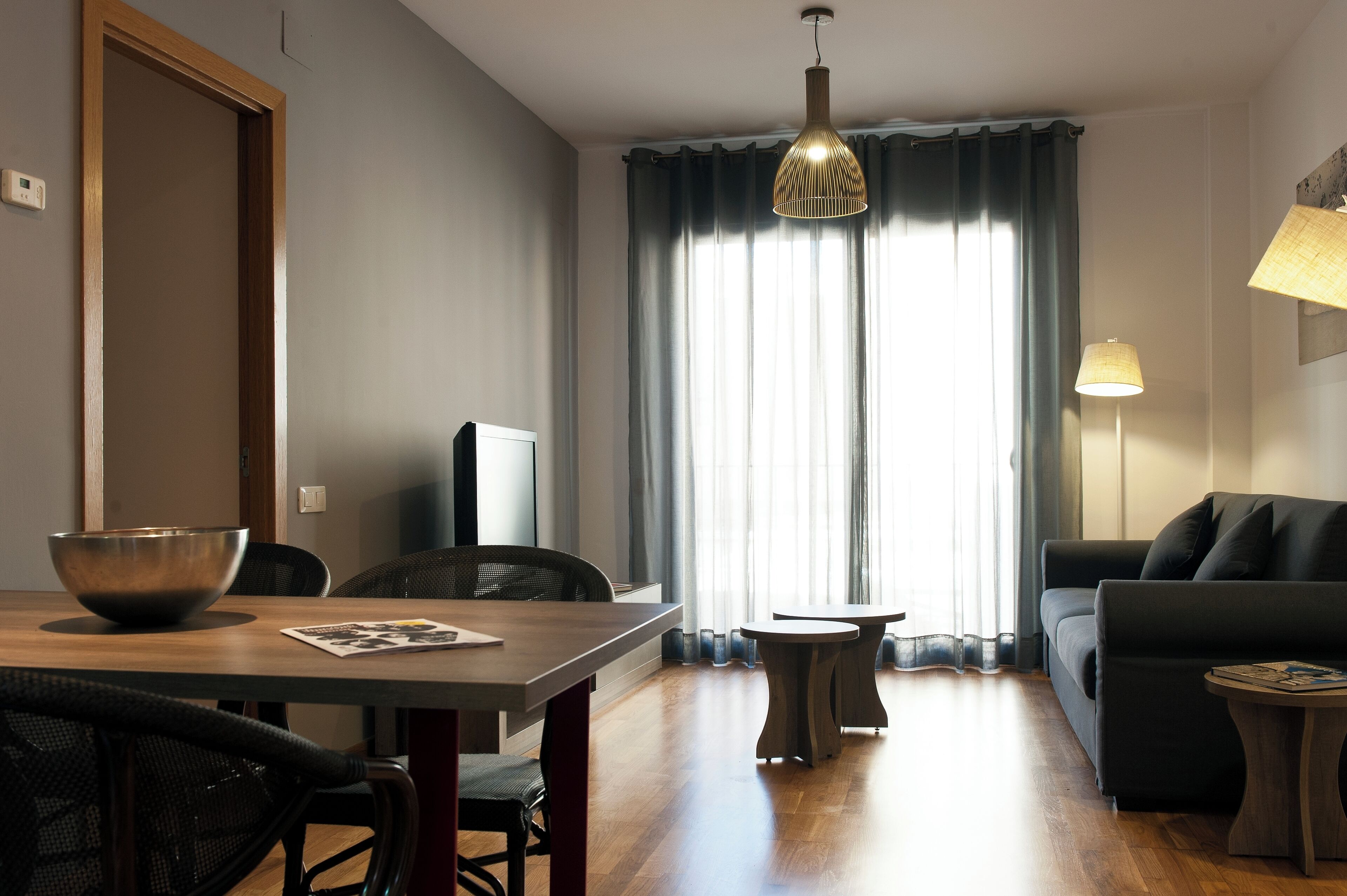 Una sala moderna con comedor, sofá, televisor y un ventanal con cortinas.