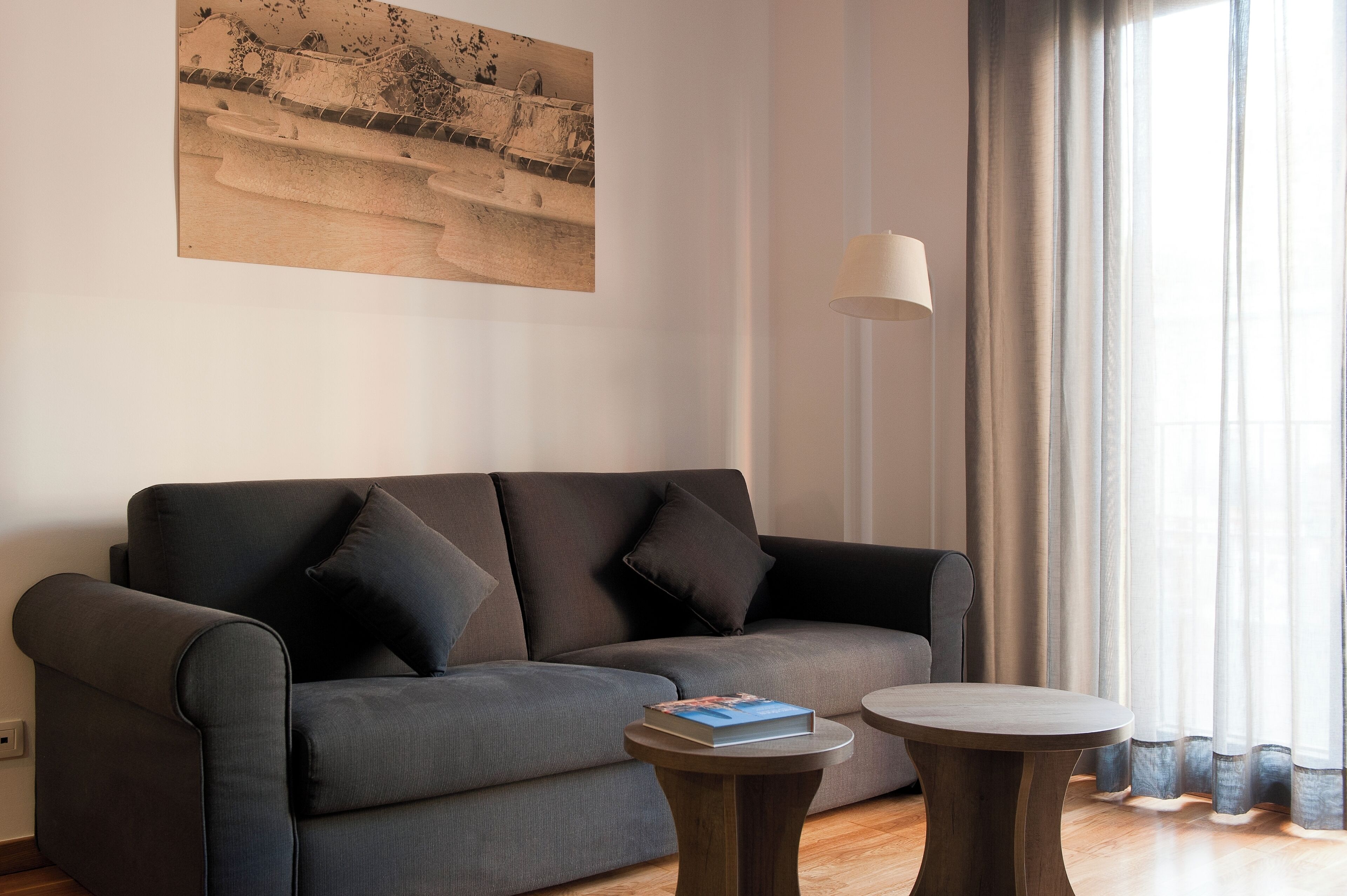 A modern living room with a grey sofa, two round side tables, a floor lamp, and a painting on the wall.