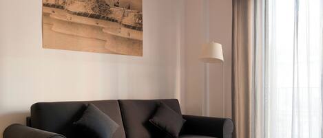 A modern living room with a grey sofa, two round side tables, a floor lamp, and a painting on the wall.