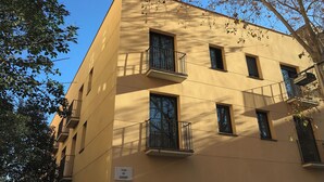 Un immeuble à plusieurs étages doté de balcons, un ciel d’un bleu éclatant et des arbres.