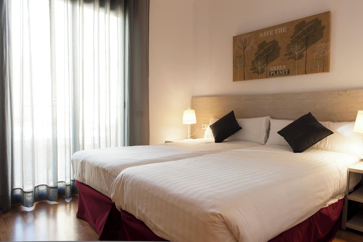 A double bed with white linens, two bedside tables with lamps, and a wall-mounted artwork with trees and the text "SAVE THE GREEN PLANET."