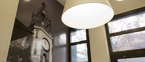 A room with a large clock tower mural, a window with a view of trees, and a hanging light fixture.