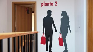 Un couloir avec une rambarde en bois, une porte portant le numéro « 1 », et un mur orné d’une fresque représentant la silhouette d’un couple tenant des sacs.