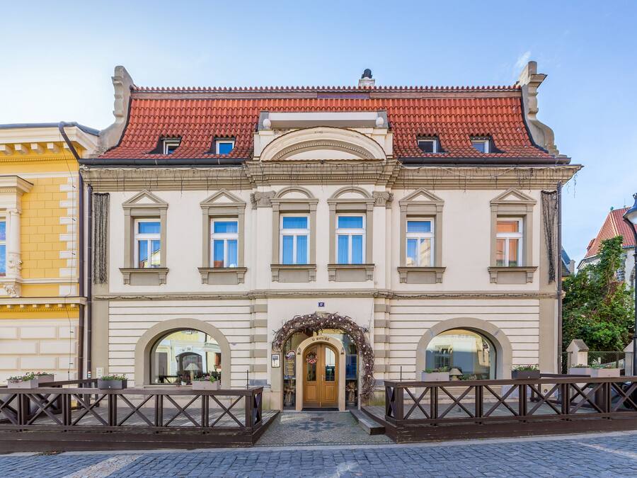Ein historisches Gebäude mit rotem Ziegeldach, rundbogigem Eingang und einer zentralen Tür, die von einem dekorativen Bogen eingefasst wird.