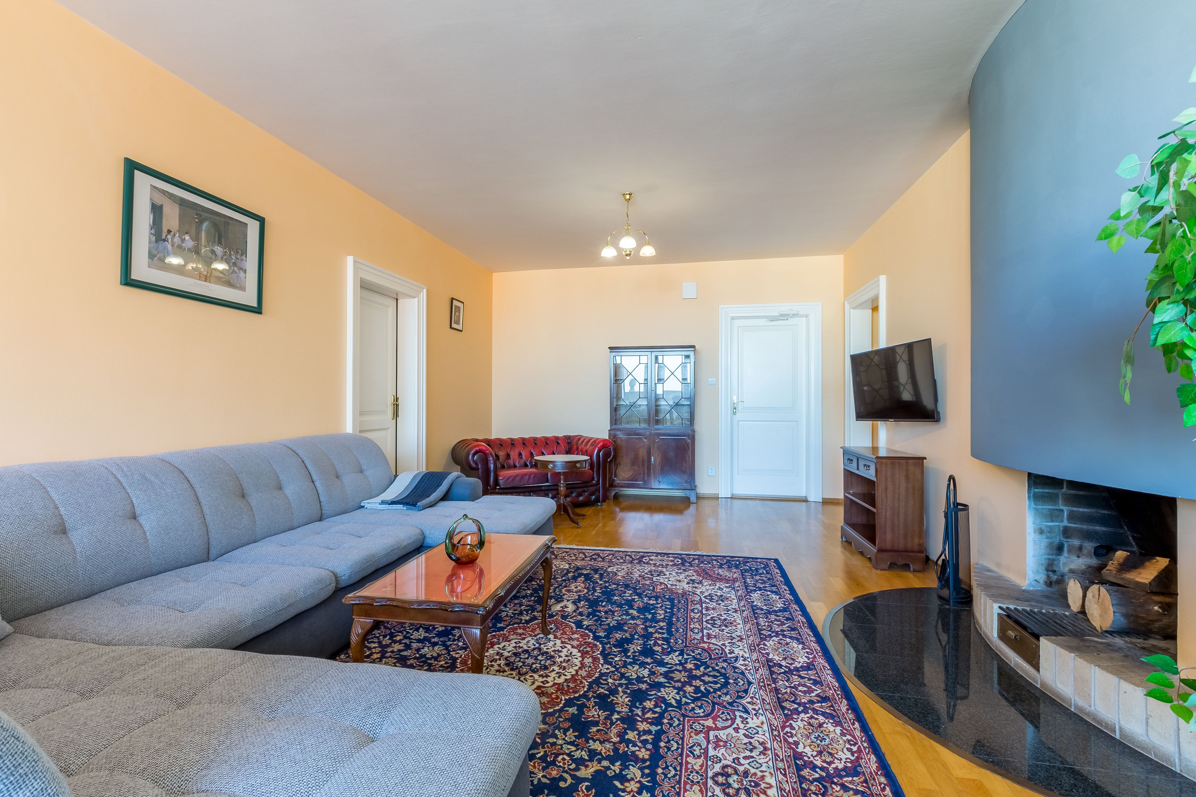 A living room with a grey sofa, a red armchair, a coffee table, a patterned rug, and a fireplace.