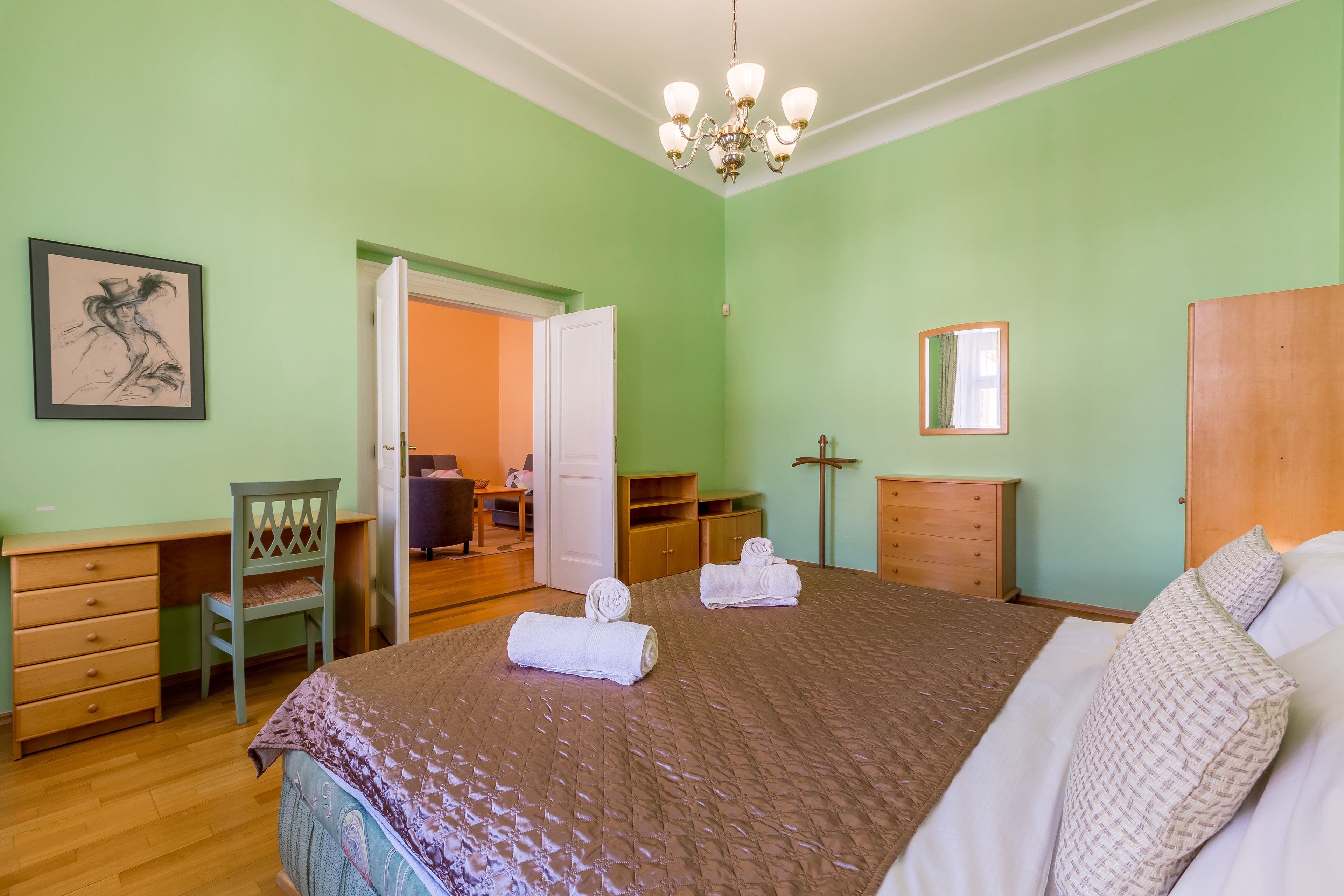A bedroom with a bed, a desk, a chair, a wardrobe, and a door leading to another room.
