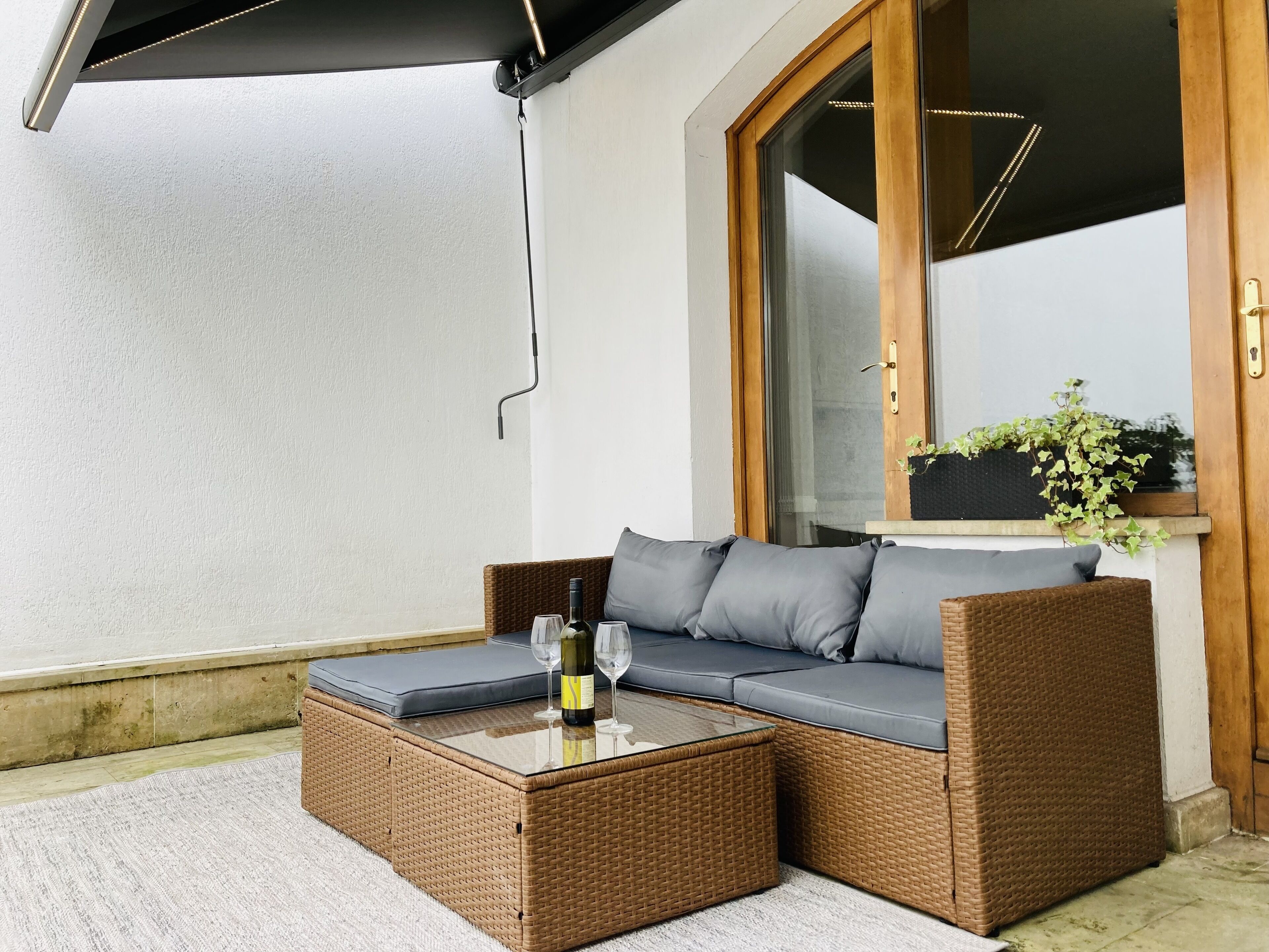Un canapé en osier avec des coussins, une table basse avec un plateau en verre et une bouteille de vin.