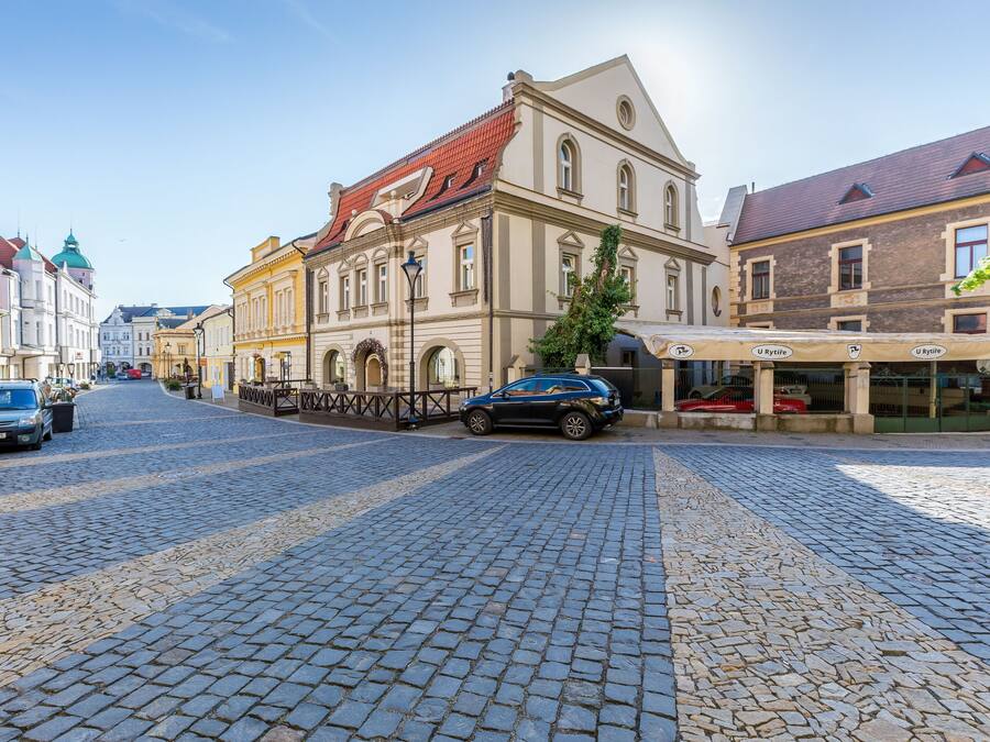 A cobblestone street lined with historic buildings, a parked car, and a visible storefront with signage.
