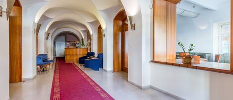 Un hall de hotel con alfombra roja, arcos de madera y una mesa de recepción.