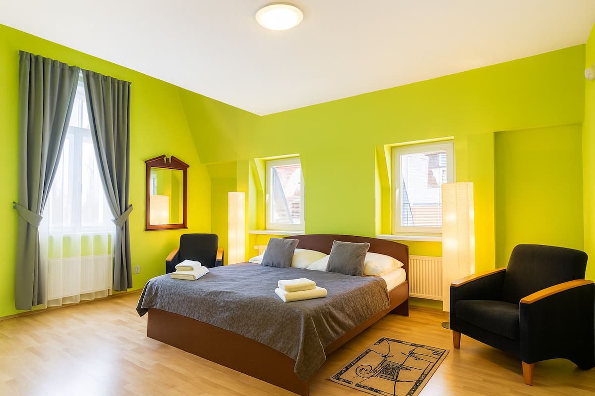 Una habitación luminosa con una cama, dos sillas, un ventanal y un espejo.