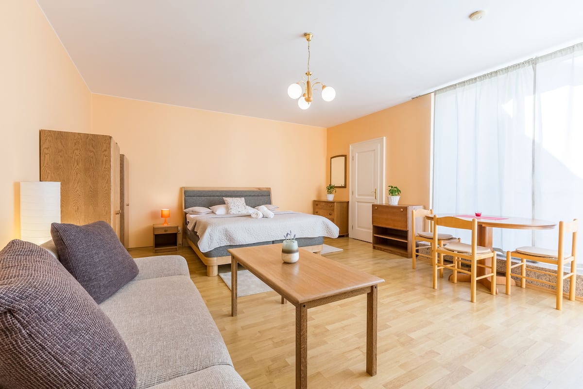 Una habitación de hotel moderna con una cama, sofá, mesa de madera y un comedor con sillas.