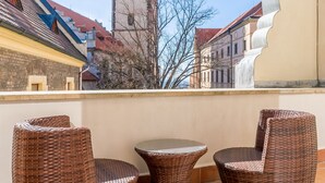 Een balkon met rieten meubilair en uitzicht op een historisch gebouw met een klokkentoren.