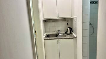 Een compacte keuken met witte kastjes, een roestvrijstalen spoelbak en een waterkoker op het aanrecht.