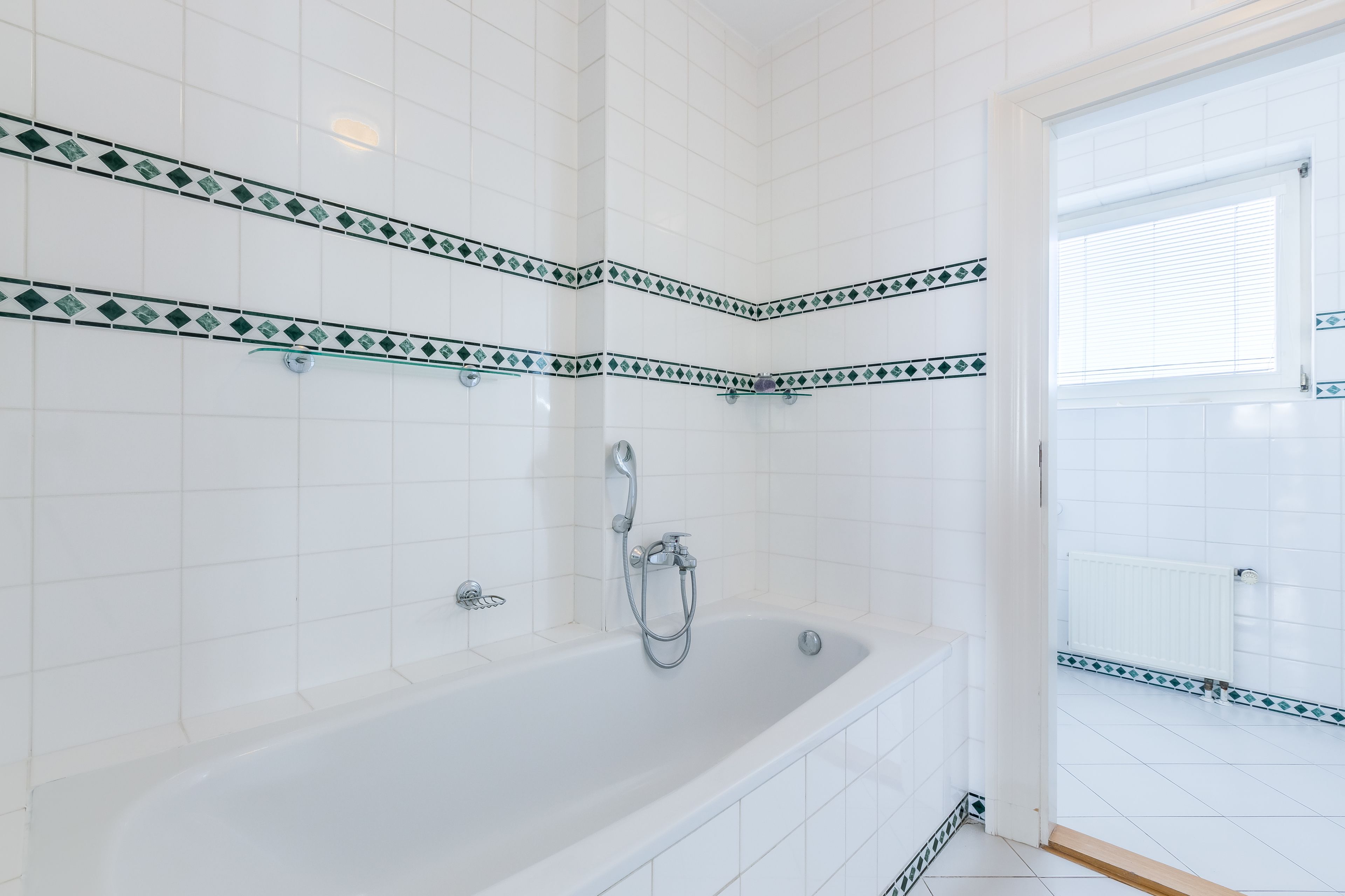 A modern bathroom with white tiles, a bathtub, and a shower area.