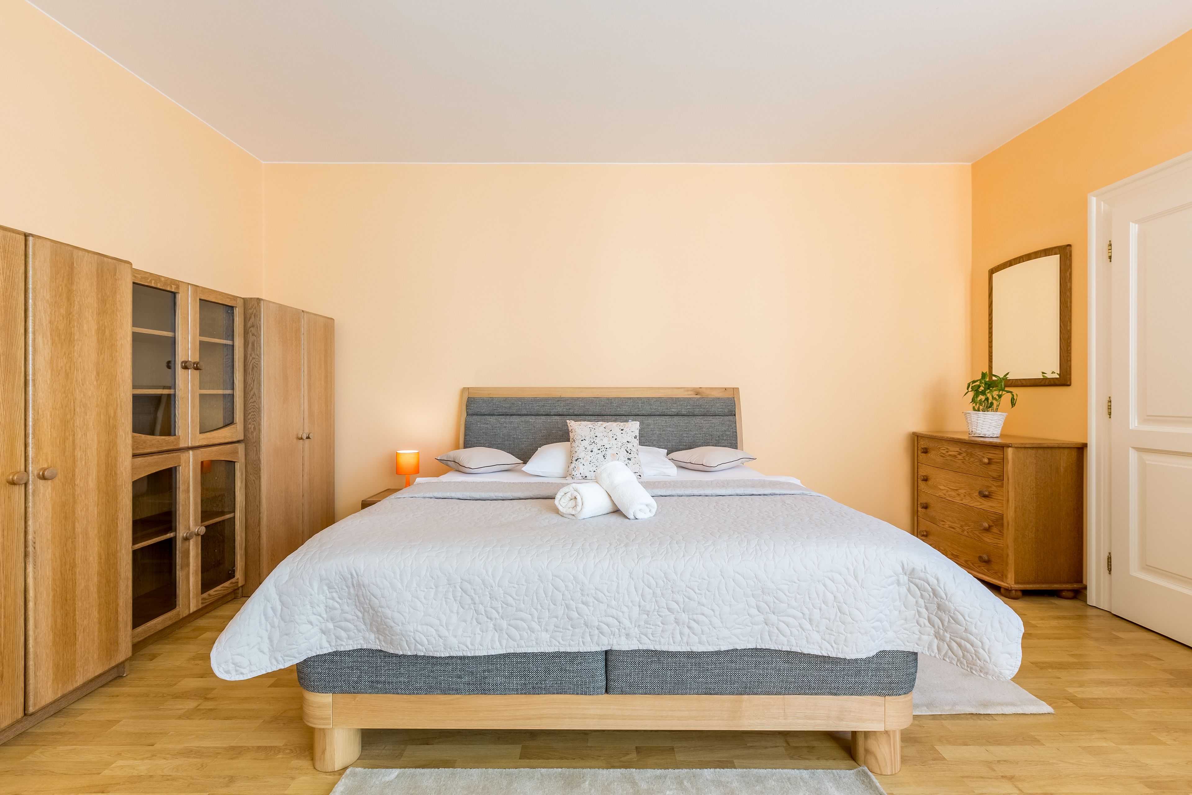 A bedroom with a bed, wooden wardrobe, bedside table, and a mirror.