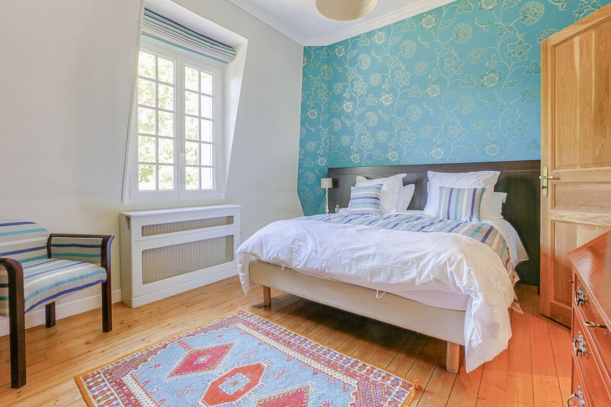 Een slaapkamer met een bed, een stoel, een radiator, een raam en een kledingkast.