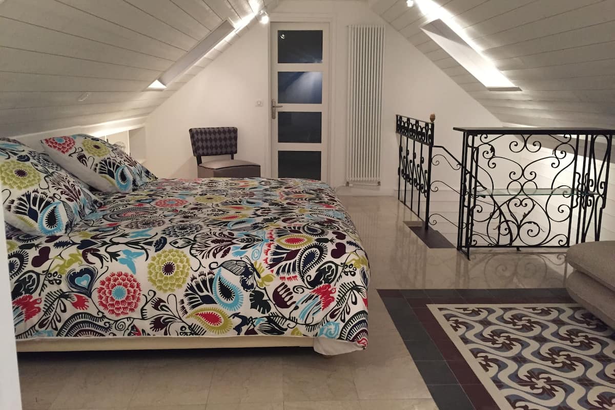 Een slaapkamer met een groot bed, een stoel, een raam, een radiator en een balkongevel.