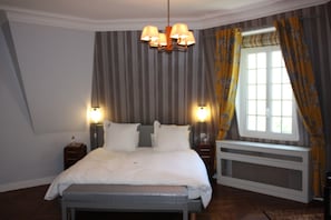 A bedroom with a bed, bedside lamps, a radiator, and a window with curtains. - Château d'Avesnes Le Castelet (Avesnes-en-Bray)