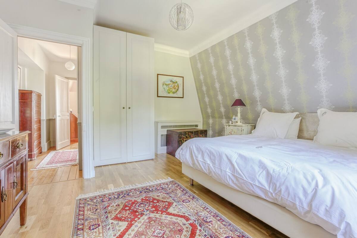 Een slaapkamer met een groot bed, een kledingkast, een bureau en een kamerkleed met een patroon.
