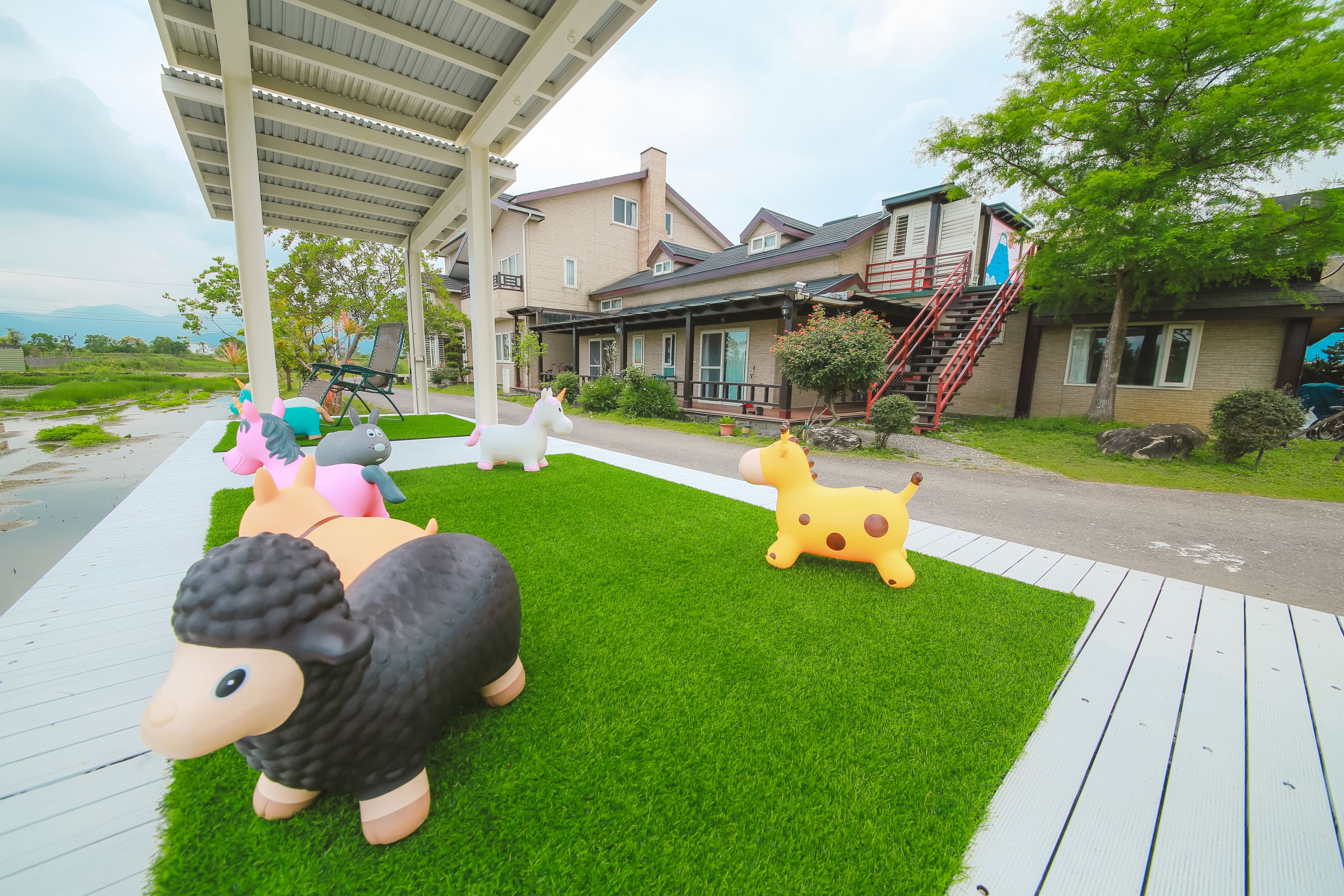 Een woonwijk met een overdekt terras, een huis met een rode trap en een gazon met grote dierenbeelden.